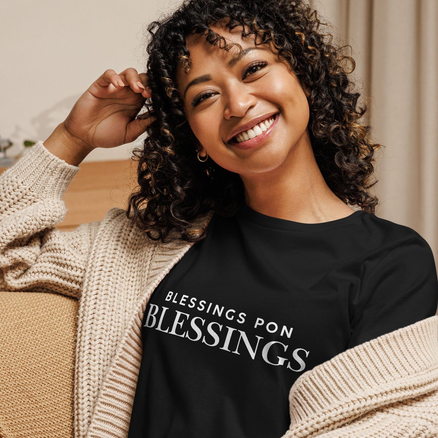 Woman wearing a black sweatshirt with 'BLESSINGS PON BLESSINGS' text, sitting on a couch.