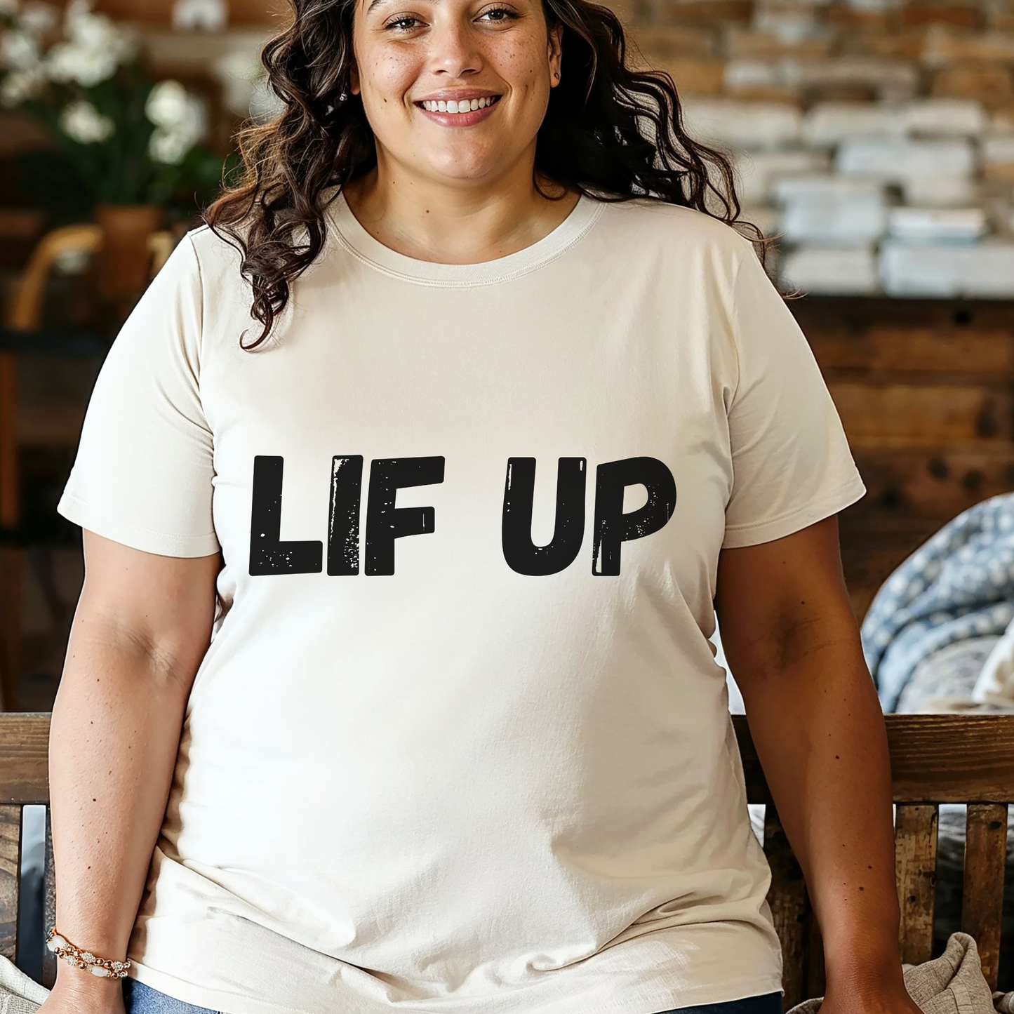 Woman wearing a beige t-shirt with 'LIF UP' text in a casual setting.