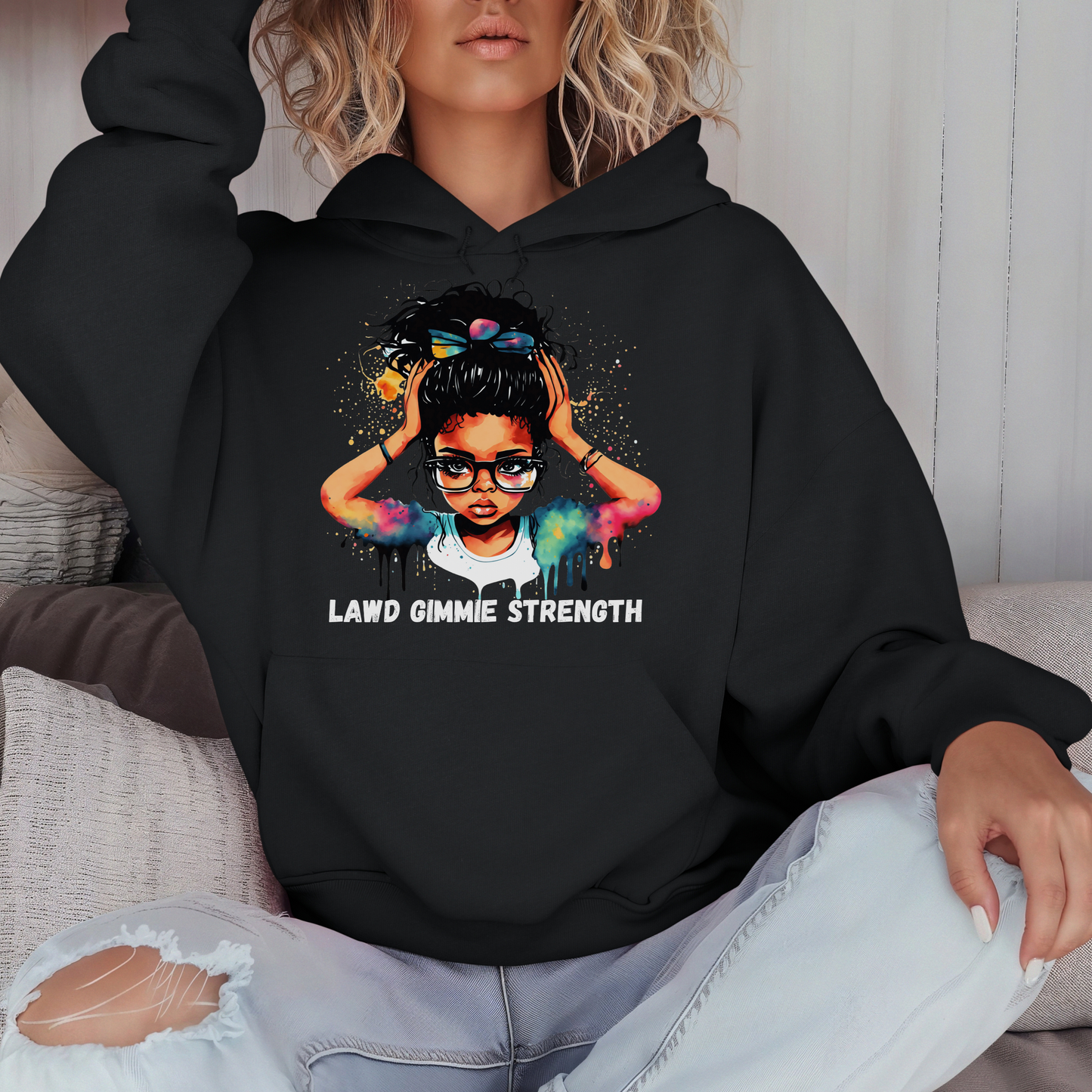 Person wearing a black hoodie with a graphic design and text, sitting on a couch.