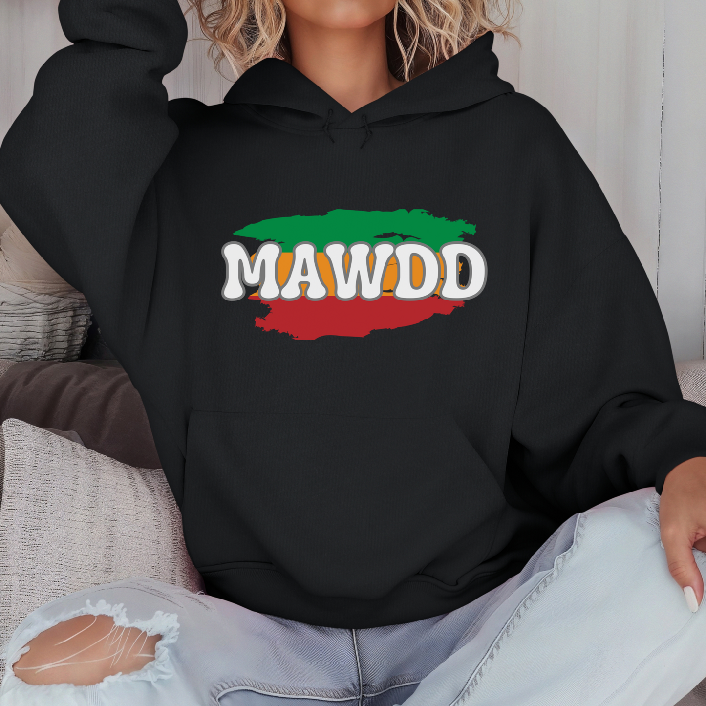 Person wearing a black hoodie with 'MAWDD' design sitting on a couch.