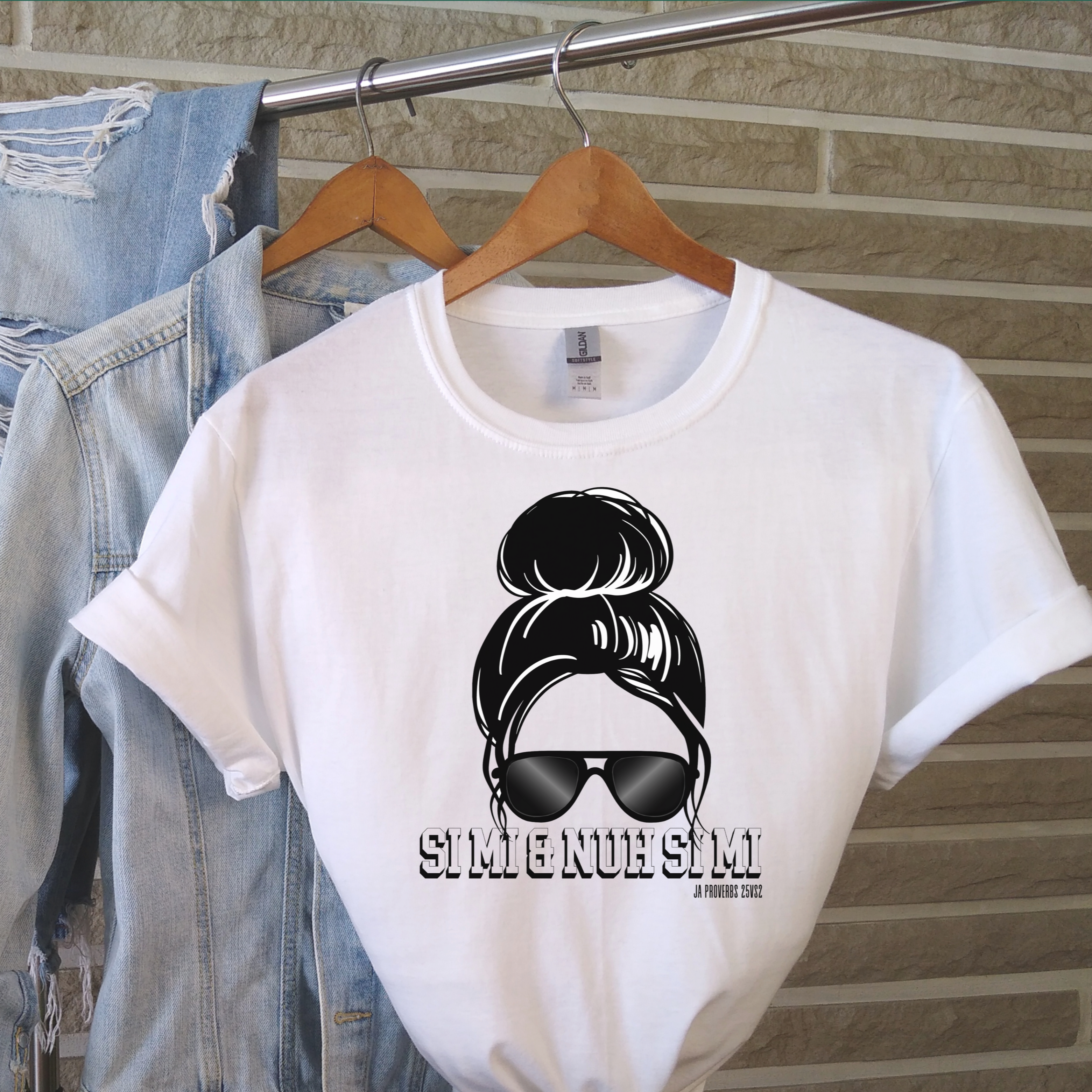 White t-shirt with graphic design and text on a hanger against a brick wall.