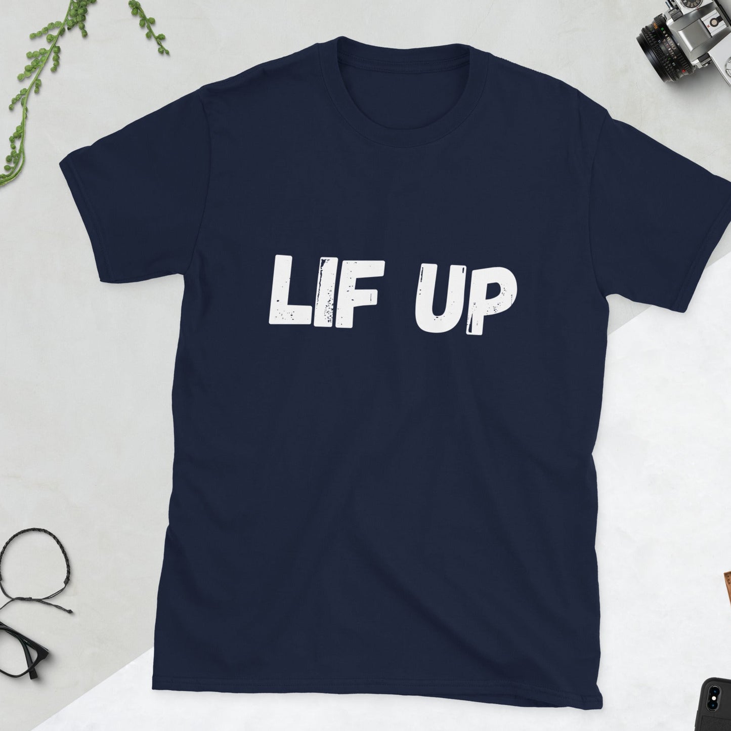 Navy blue t-shirt with 'LIF UP' text on a light gray surface with casual items around.