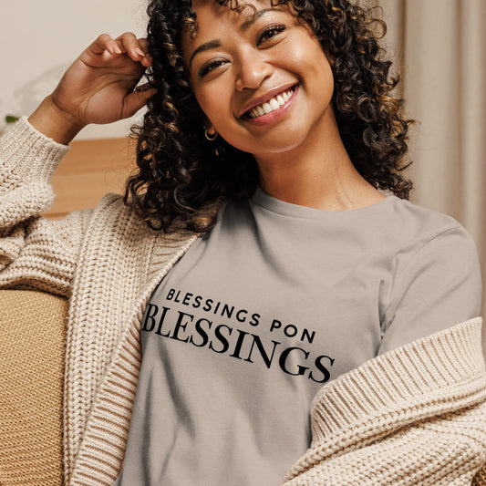 Woman wearing a heather stone t-shirt with 'BLESSINGS PON BLESSINGS' text, sitting on a couch.