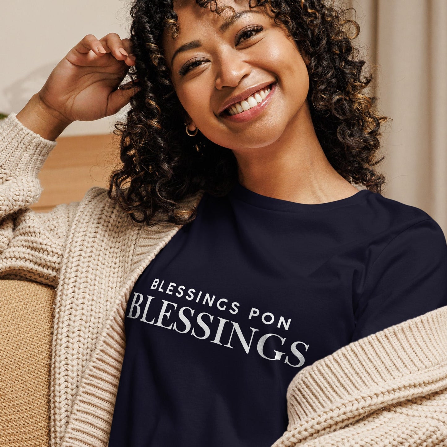 Woman wearing a navy blue sweatshirt with 'BLESSINGS PON BLESSINGS' text, sitting on a couch.